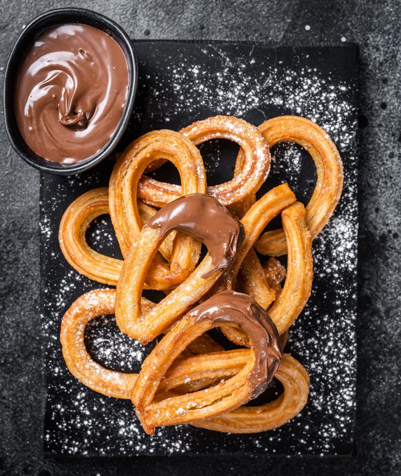 Vista desde arriba de Churros con chocolate sobre una pizarra negra.